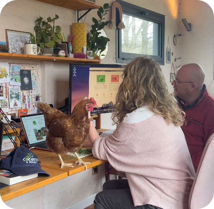 Roxane qui travaille sur son ordinateur avec un client, avec une poule en premier plan qui se tient sur le bureau